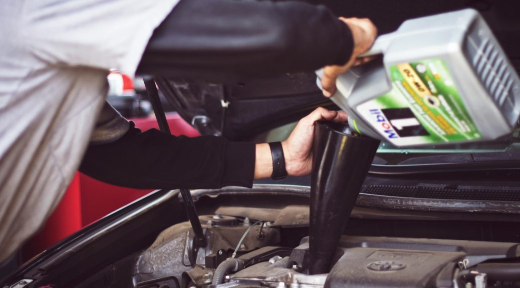 man refilling motor oil on car engine bay